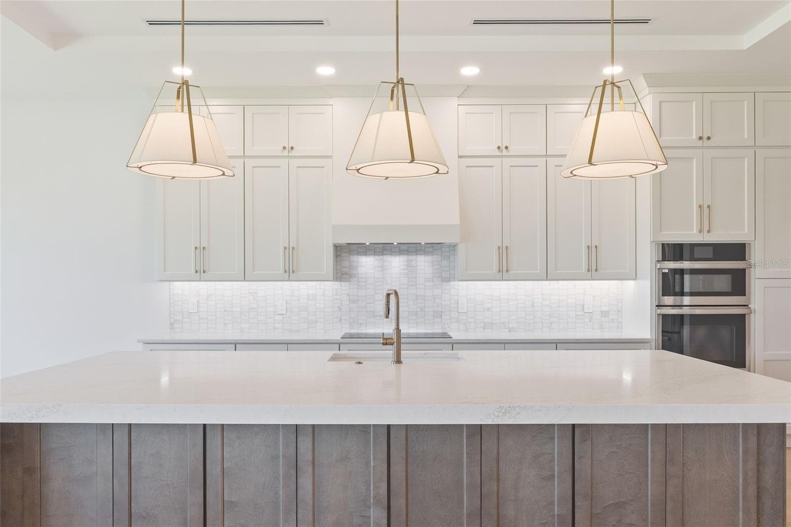 The gourmet kitchen is a true showpiece, featuring full-height custom cabinetry, an oversized 11-foot quartz island with storage on both sides, marble backsplash, GE Profile appliances, custom range hood, cooktop, wall oven, and soft-close cabinetry throughout. - 1336 HAYS RD, TARPON SPRINGS