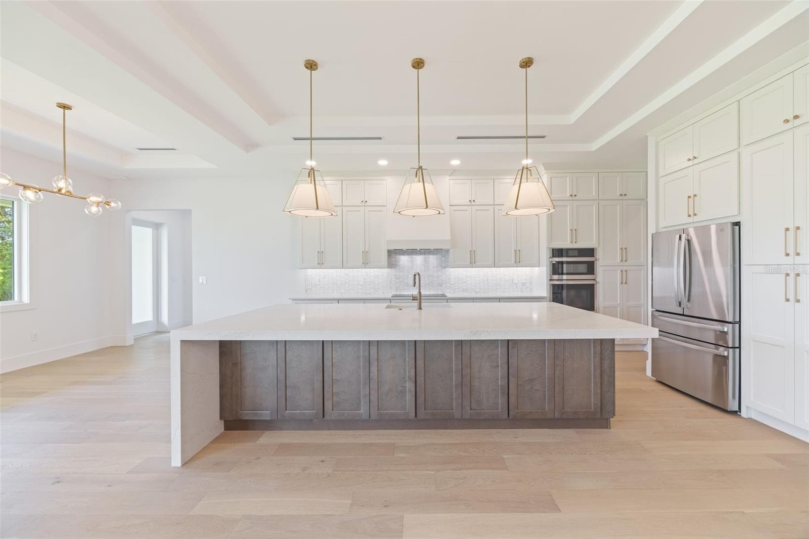 The gourmet kitchen is a true showpiece, featuring full-height custom cabinetry, an oversized 11-foot quartz island with storage on both sides, marble backsplash, GE Profile appliances, custom range hood, cooktop, wall oven, and soft-close cabinetry throughout. - 1336 HAYS RD, TARPON SPRINGS