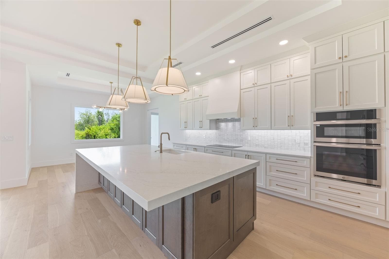 The gourmet kitchen is a true showpiece, featuring full-height custom cabinetry, an oversized 11-foot quartz island with storage on both sides, marble backsplash, GE Profile appliances, custom range hood, cooktop, wall oven, and soft-close cabinetry throughout. - 1336 HAYS RD, TARPON SPRINGS