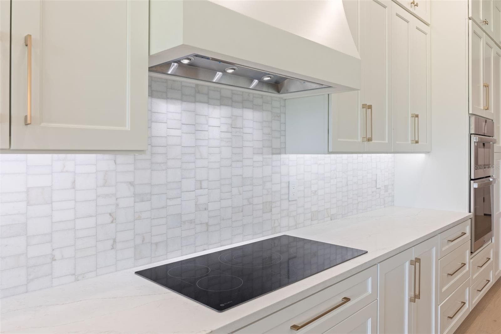 The gourmet kitchen is a true showpiece, featuring full-height custom cabinetry, an oversized 11-foot quartz island with storage on both sides, marble backsplash, GE Profile appliances, custom range hood, cooktop, wall oven, and soft-close cabinetry throughout. - 1336 HAYS RD, TARPON SPRINGS