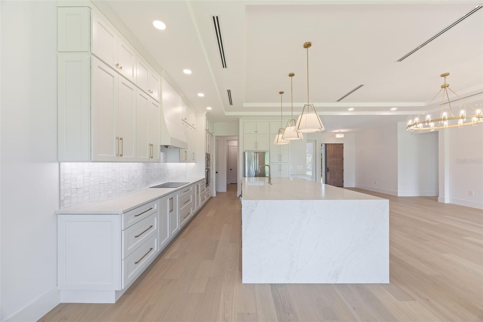The gourmet kitchen is a true showpiece, featuring full-height custom cabinetry, an oversized 11-foot quartz island with storage on both sides, marble backsplash, GE Profile appliances, custom range hood, cooktop, wall oven, and soft-close cabinetry throughout. - 1336 HAYS RD, TARPON SPRINGS