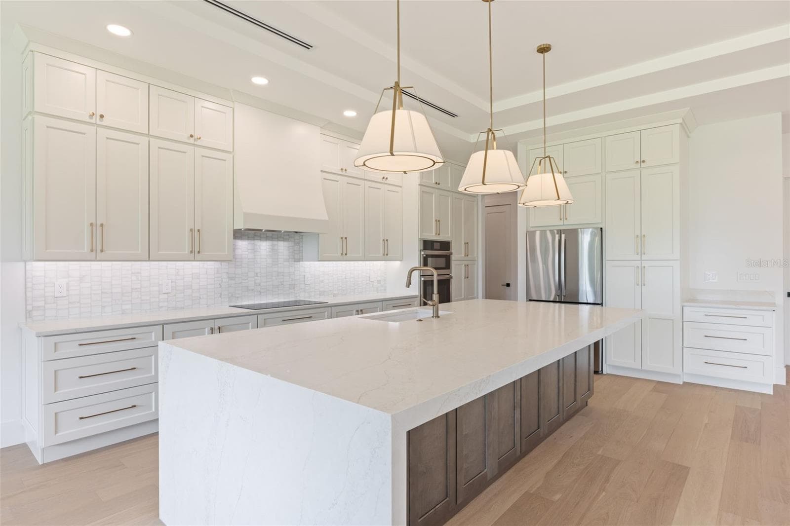 The gourmet kitchen is a true showpiece, featuring full-height custom cabinetry, an oversized 11-foot quartz island with storage on both sides, marble backsplash, GE Profile appliances, custom range hood, cooktop, wall oven, and soft-close cabinetry throughout. - 1336 HAYS RD, TARPON SPRINGS