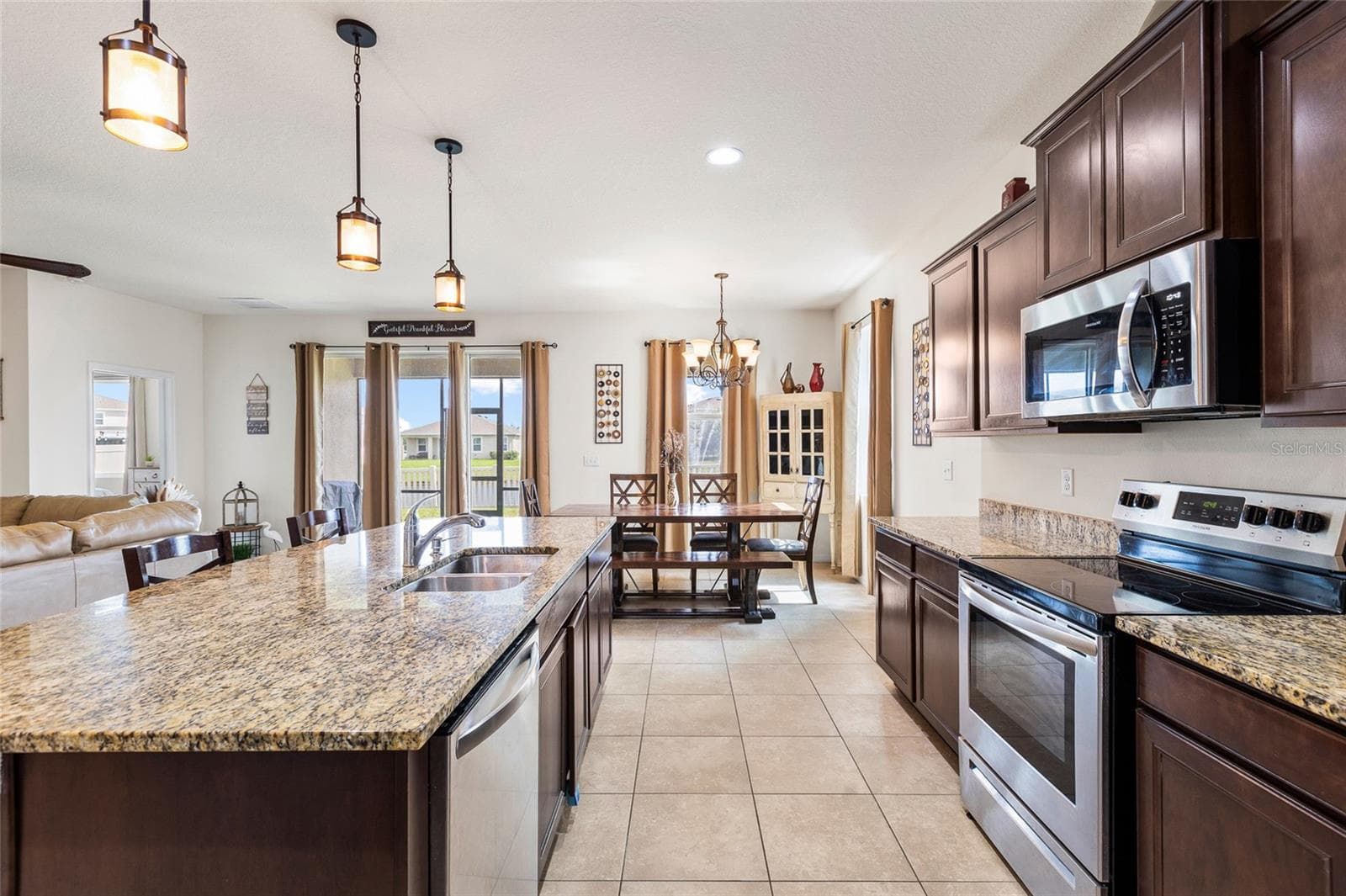 The heart of the home is the spacious open-concept kitchen, designed for both everyday living and entertaining. Features include granite countertops, a large center island with breakfast bar seating, stainless steel appliances, 36-inch cabinetry, a corner pantry, and abundant counter space. The kitchen seamlessly connects to the dining and living areas, creating a bright and functional gathering space. - 5025 JACKEL CHASE DR, WIMAUMA