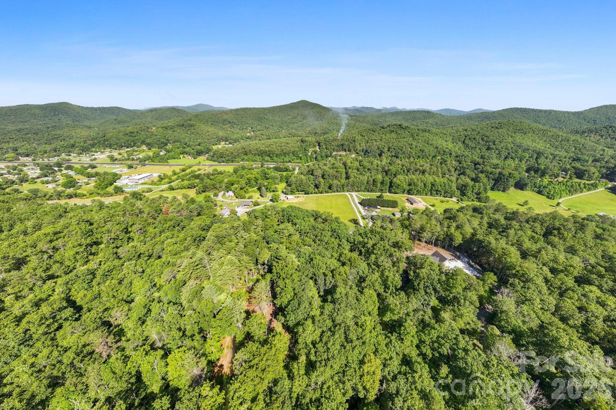 An aerial showcase of the property's incredible layout. This bird's-eye view highlights the sheer scale of the great pasture bordered by mature trees and neighboring farms. - Pisgah Forest