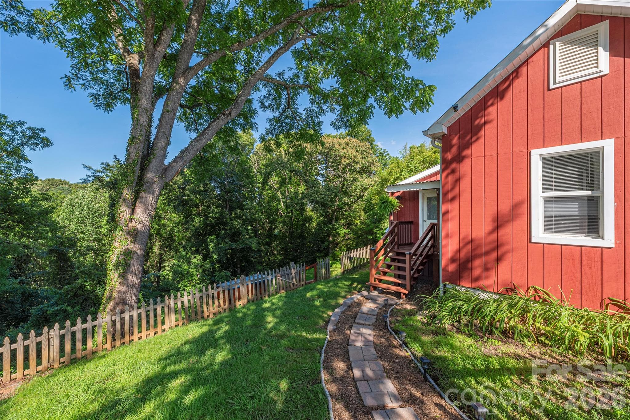 New stone walkway leads to the side entrance, surrounded by mature landscaping. - Canton