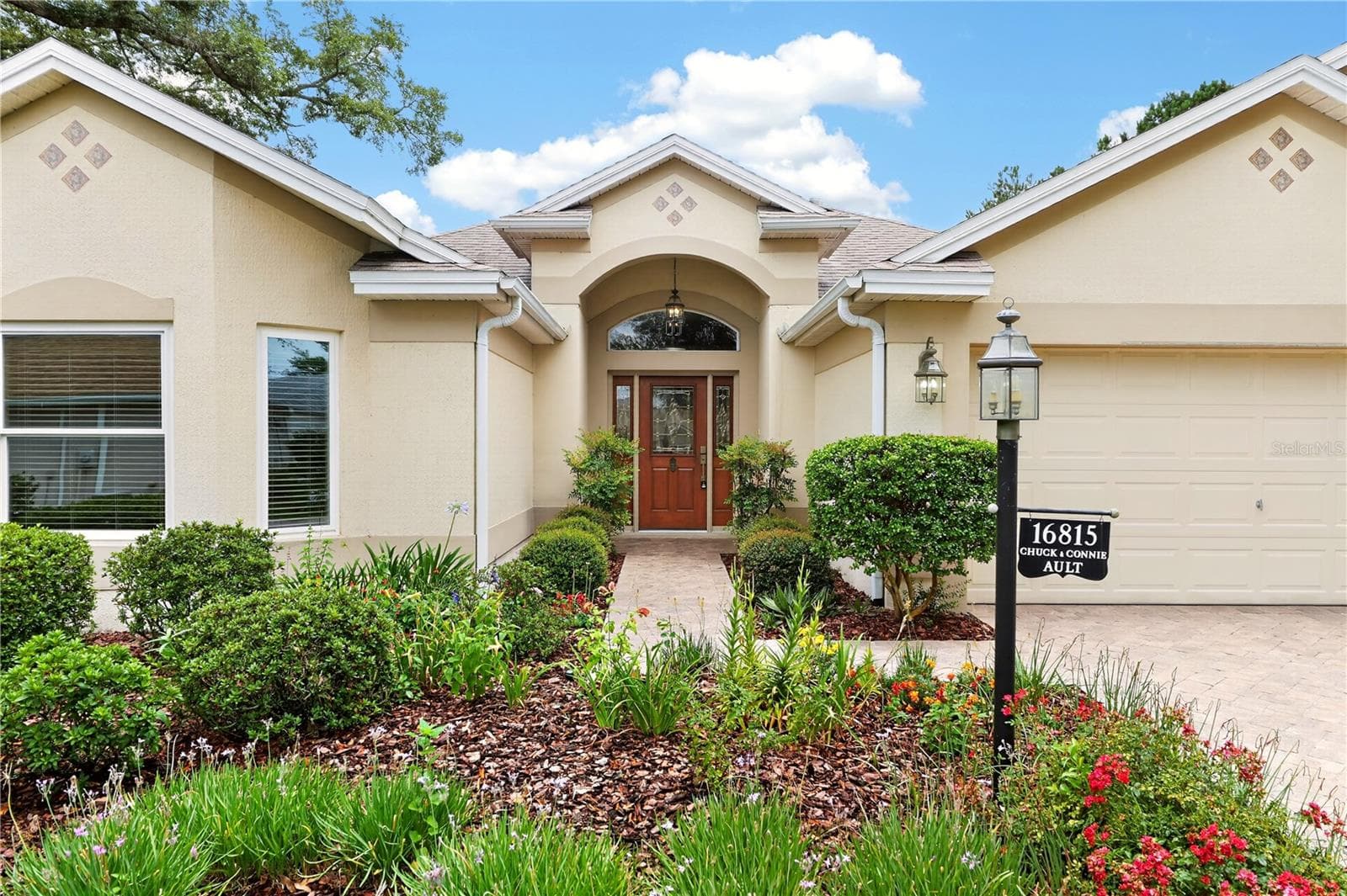Inviting front entry featuring an arched covered entrance, glass front door, and lush garden beds. - 16815 SE 85TH BELKNAP AVE, THE VILLAGES
