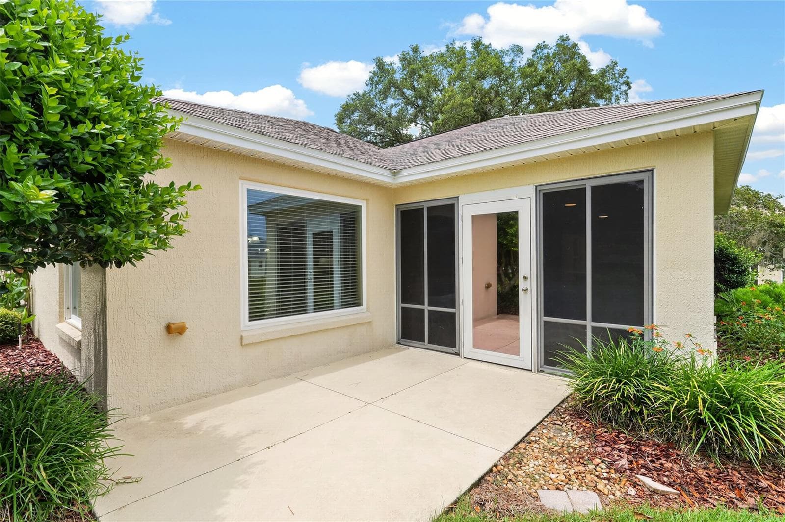 Rear patio area with access from the enclosed lanai, surrounded by mature landscaping and easy outdoor living space. - 16815 SE 85TH BELKNAP AVE, THE VILLAGES