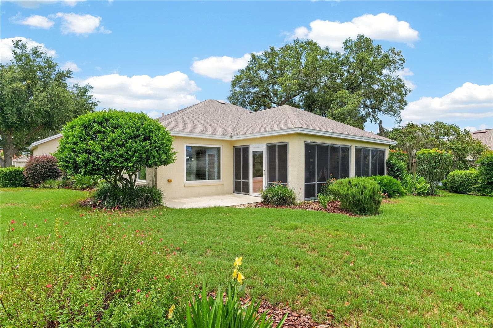 Rear exterior view highlighting the enclosed lanai, spacious lawn, and serene golf course-style setting. - 16815 SE 85TH BELKNAP AVE, THE VILLAGES