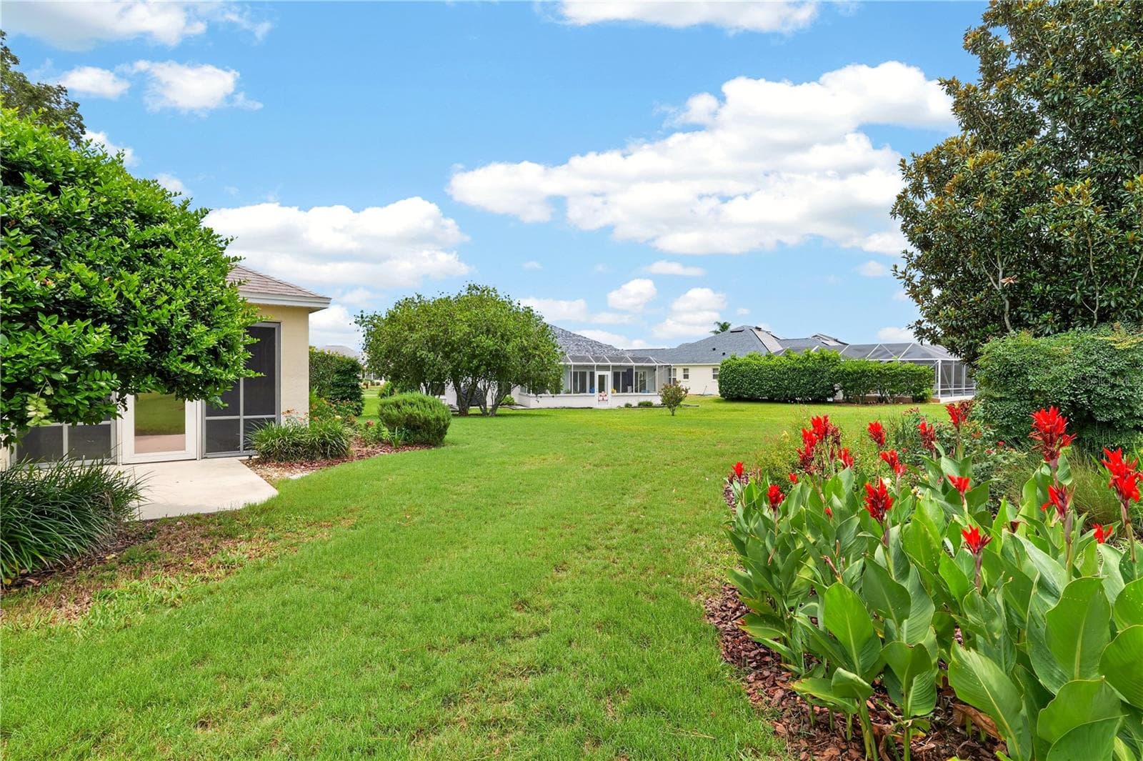 Spacious backyard setting with lush green lawn, colorful landscaping, and peaceful open views. - 16815 SE 85TH BELKNAP AVE, THE VILLAGES