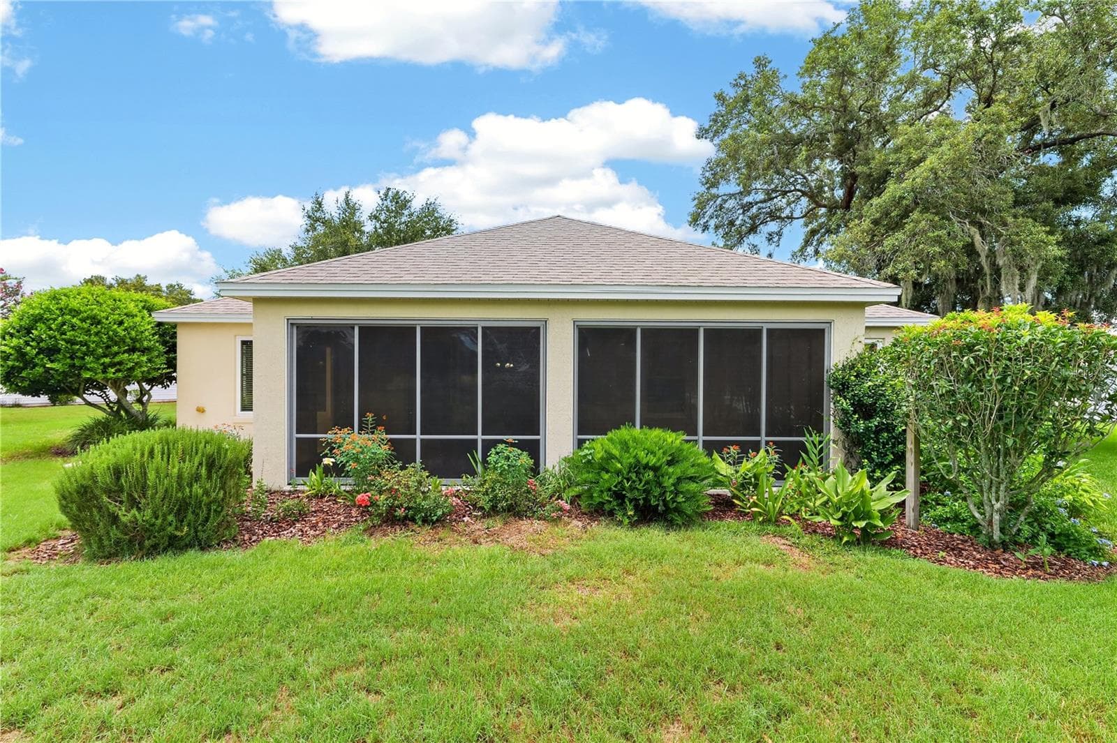 Rear exterior view highlighting the enclosed lanai, mature landscaping, and beautifully maintained lawn. - 16815 SE 85TH BELKNAP AVE, THE VILLAGES