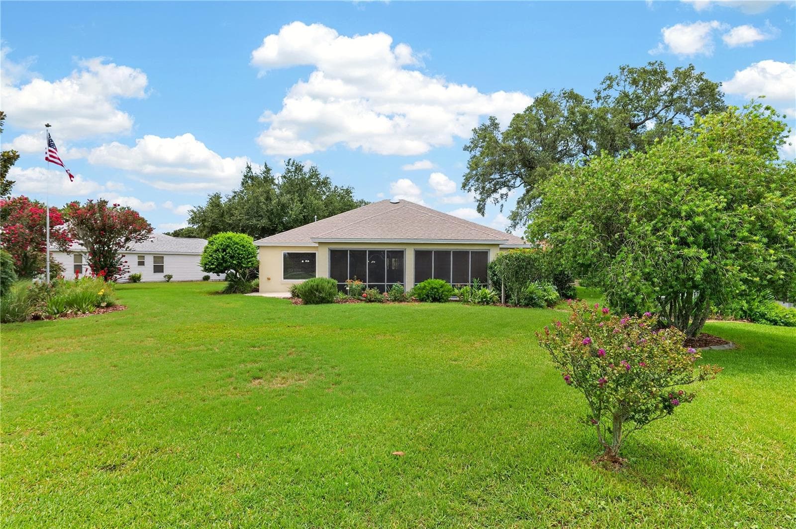 Wide backyard view highlighting the enclosed lanai, generous lawn area, and attractive surrounding landscapin - 16815 SE 85TH BELKNAP AVE, THE VILLAGES