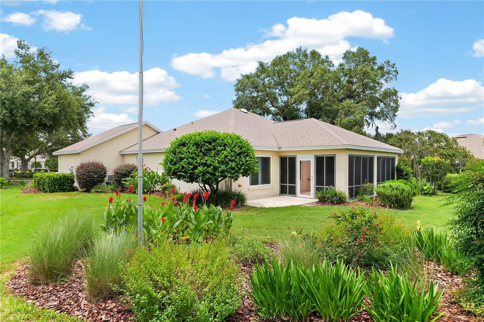 Beautiful rear exterior with lush lawn, mature plantings, and colorful garden beds framing the home. - 16815 SE 85TH BELKNAP AVE, THE VILLAGES