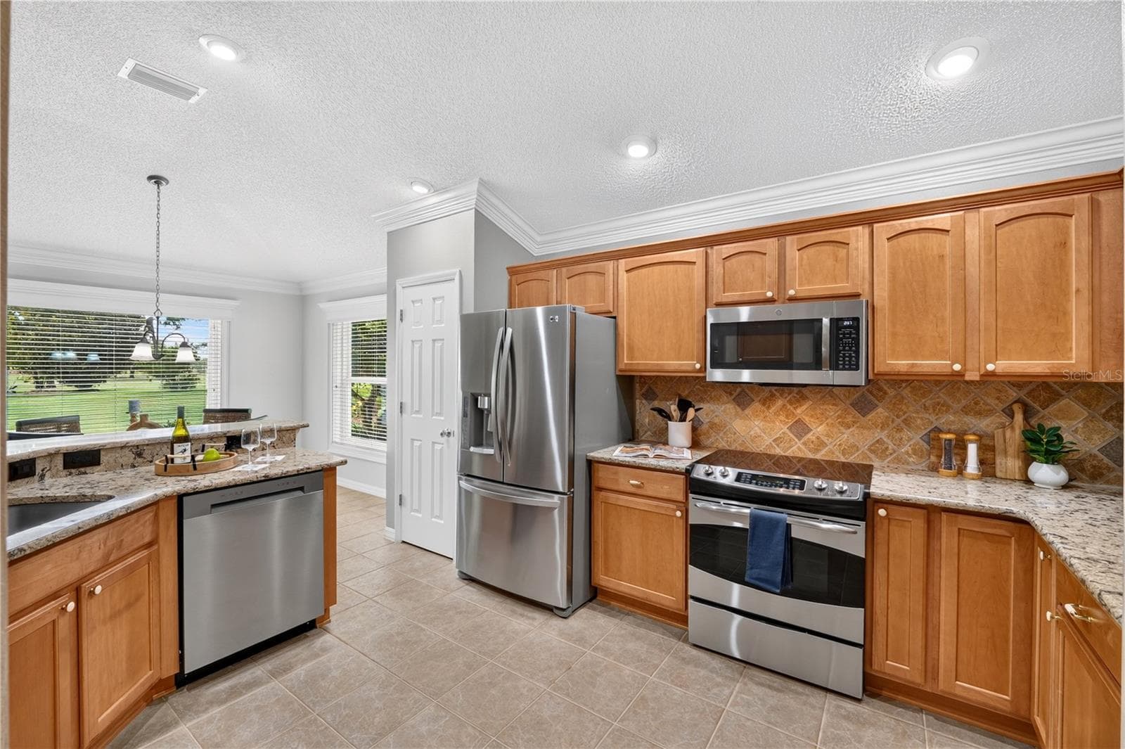 Well-appointed kitchen with wood cabinetry, stainless steel appliances, tile backsplash, and ample counter space. - 16815 SE 85TH BELKNAP AVE, THE VILLAGES