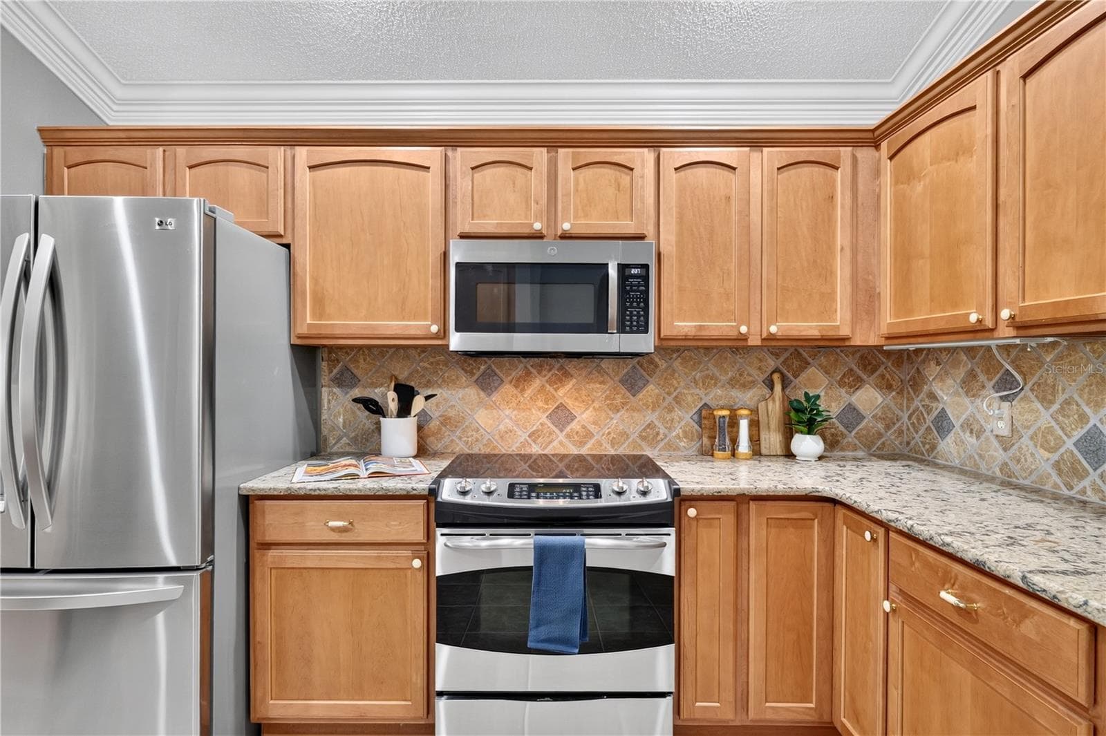 Kitchen detail featuring HIGH END stainless steel appliances, warm wood cabinetry, tile backsplash, and recessed lighting. - 16815 SE 85TH BELKNAP AVE, THE VILLAGES