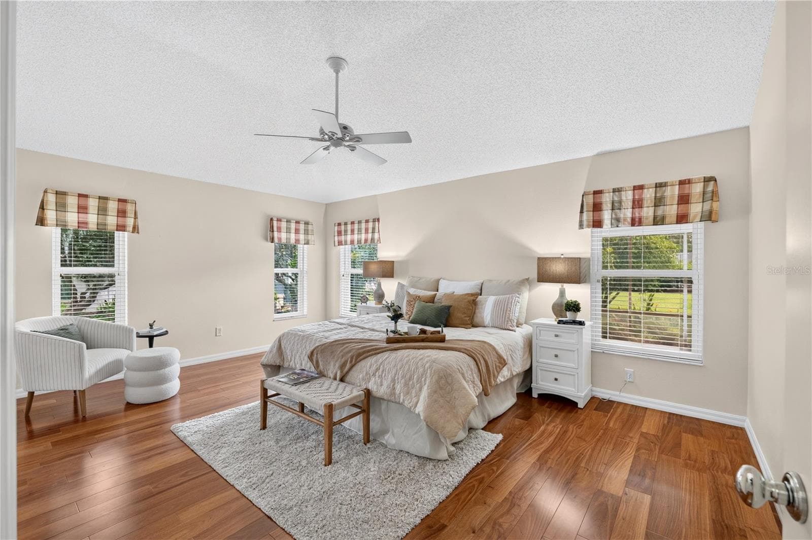 Spacious primary bedroom with high ceilings, rich wood flooring, ceiling fan, and multiple windows for natural light. - 16815 SE 85TH BELKNAP AVE, THE VILLAGES