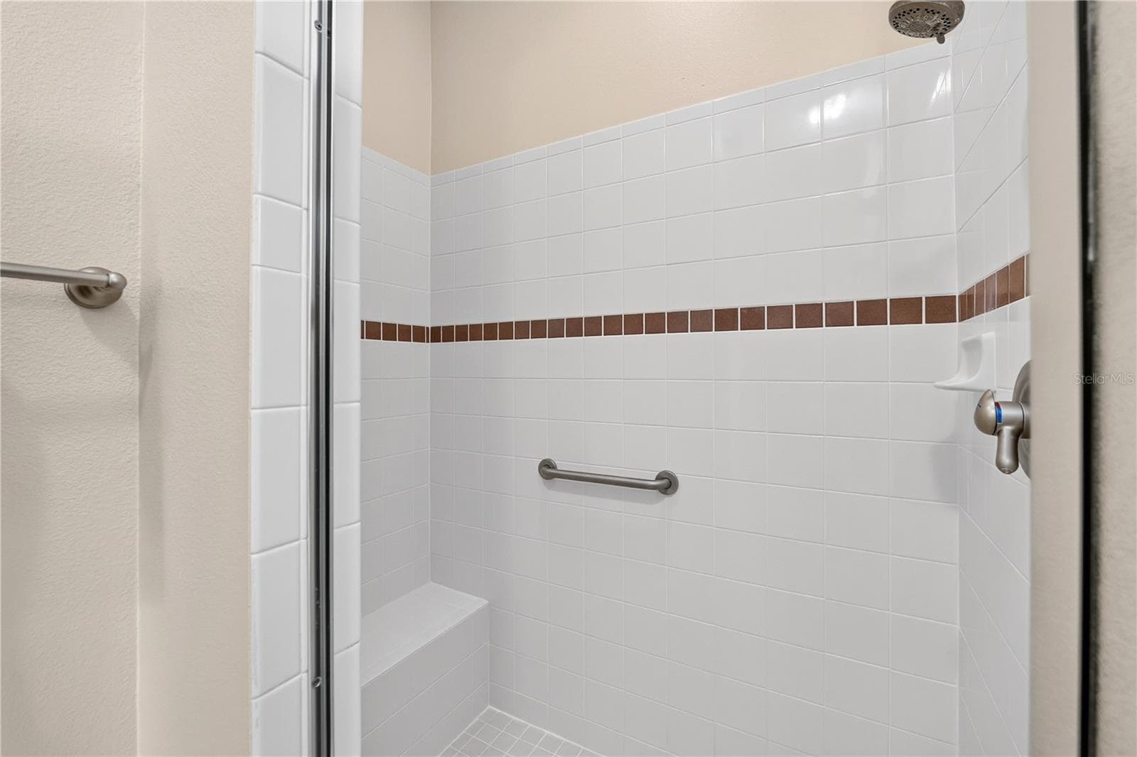 Primary shower with neutral tile surround, built-in bench, grab bar, and decorative accent detail. - 16815 SE 85TH BELKNAP AVE, THE VILLAGES
