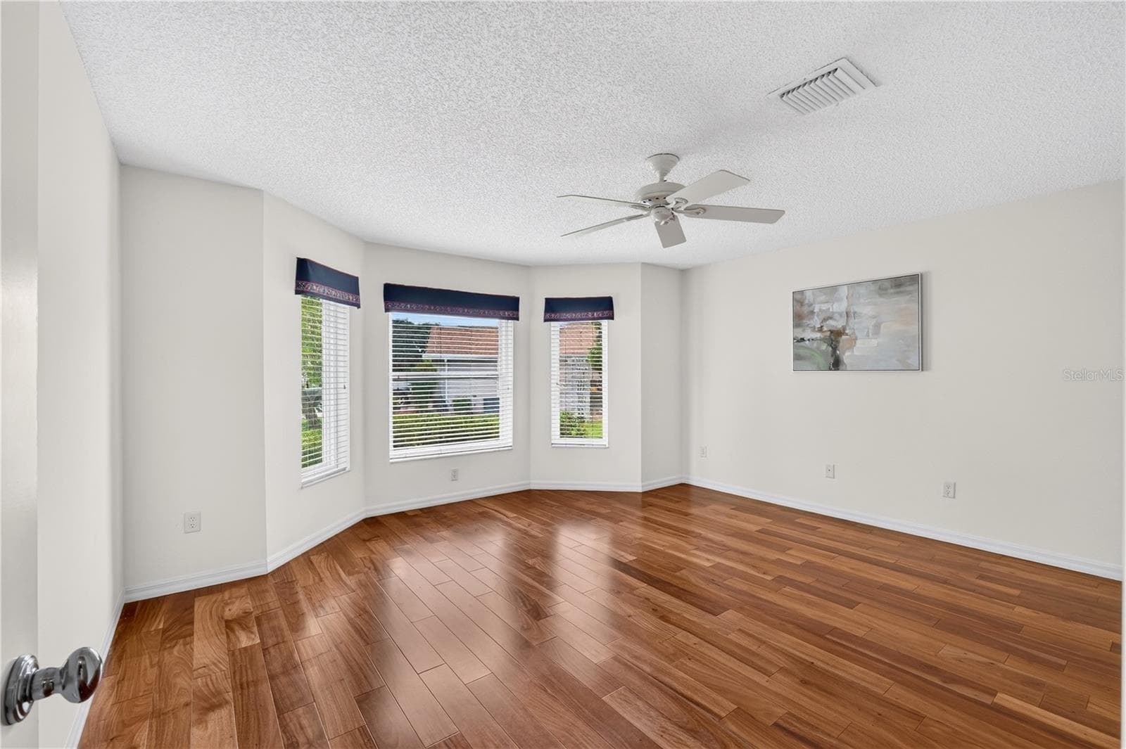 Spacious guest bedroom with wood flooring, ceiling fan, and a bay-style window area bringing in natural light. - 16815 SE 85TH BELKNAP AVE, THE VILLAGES