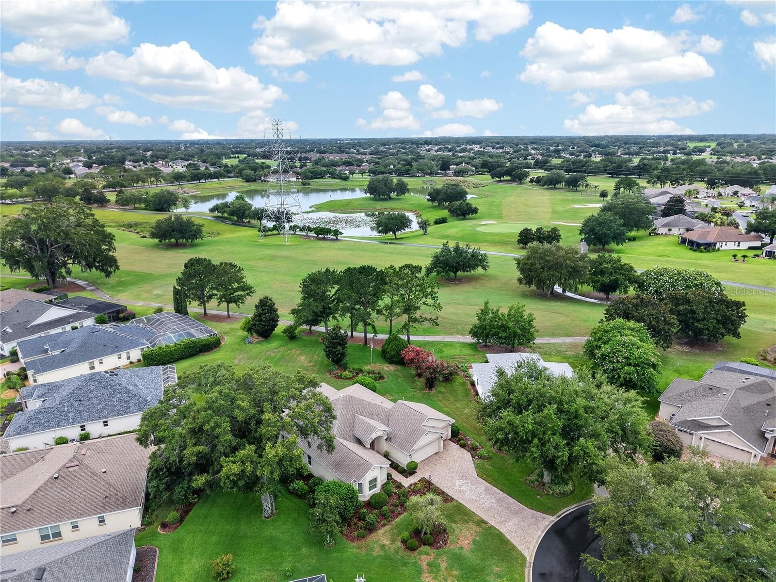 Expansive aerial view showcasing the home’s scenic golf course setting, surrounding green space, mature trees, and nearby water views. - 16815 SE 85TH BELKNAP AVE, THE VILLAGES
