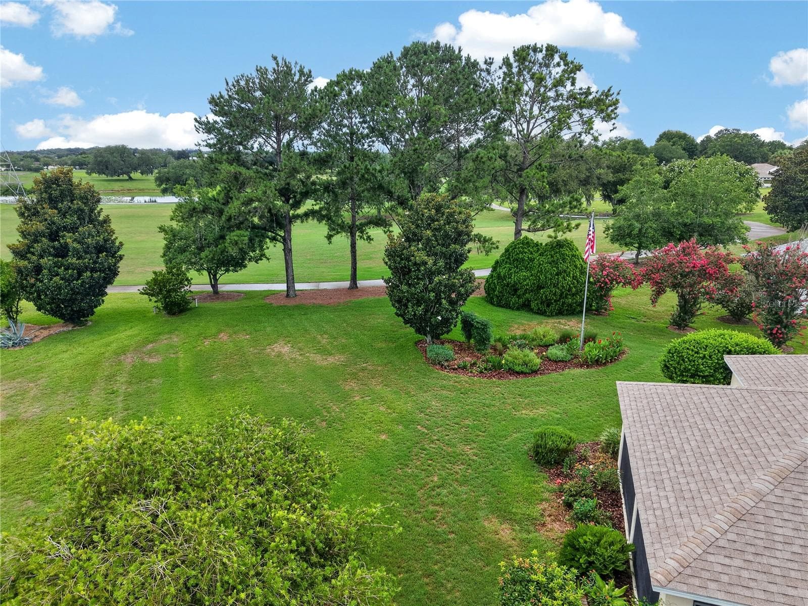Elevated backyard view featuring open green space, mature trees, colorful landscaping, and a serene setting behind the home. - 16815 SE 85TH BELKNAP AVE, THE VILLAGES
