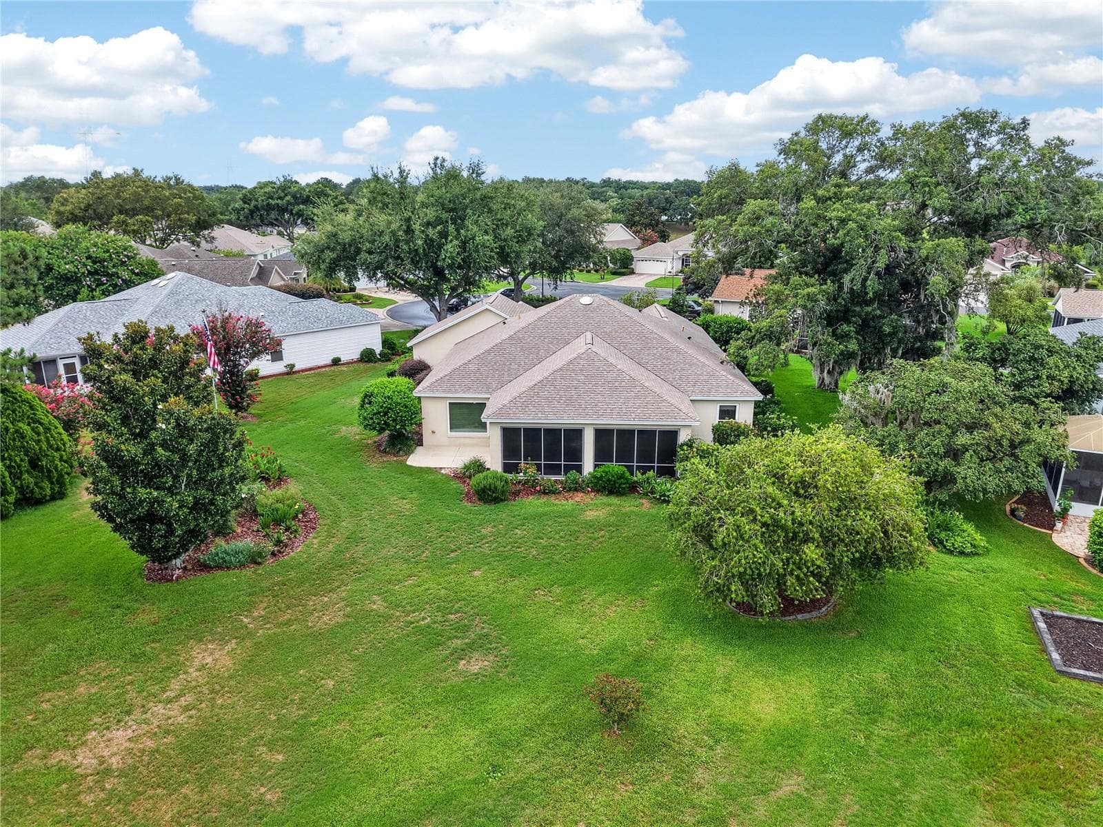 Rear aerial view showcasing the enclosed lanai, spacious lawn, mature trees, and private-feeling outdoor setting. - 16815 SE 85TH BELKNAP AVE, THE VILLAGES