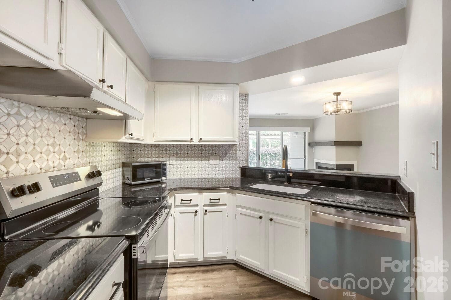 Dark granite countertops contrast beautifully with white cabinetry and a striking mosaic backsplash in this fully updated kitchen. A pass-through view to the living room's fireplace keeps the space feeling open and connected. - Charlotte