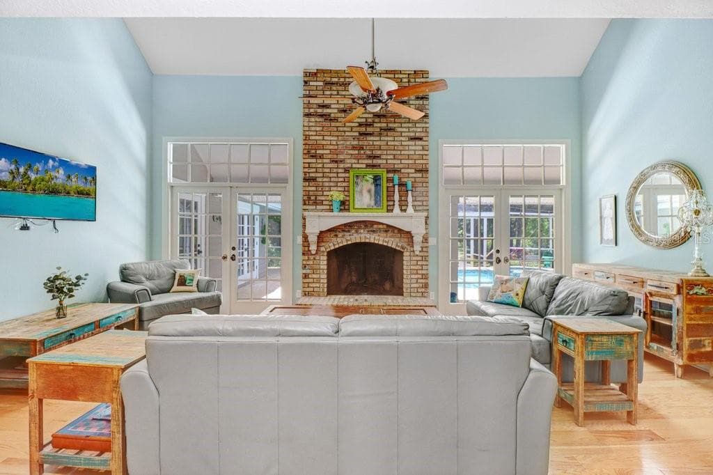 Hacienda style Great Room with hardwood floors, french doors and brick fireplace with custom mantle - 1976 DUNLOE CIR, DUNEDIN