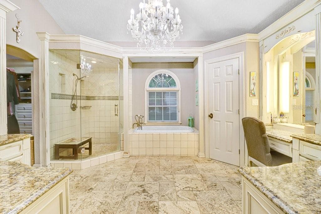 Amazing master bathroom with beautiful custom lighting and chandelier with steam shower, vanity area, large Roman soaking tub, and his and her sink areas that include custom cabinetry and granite counter tops throughout. - 1976 DUNLOE CIR, DUNEDIN
