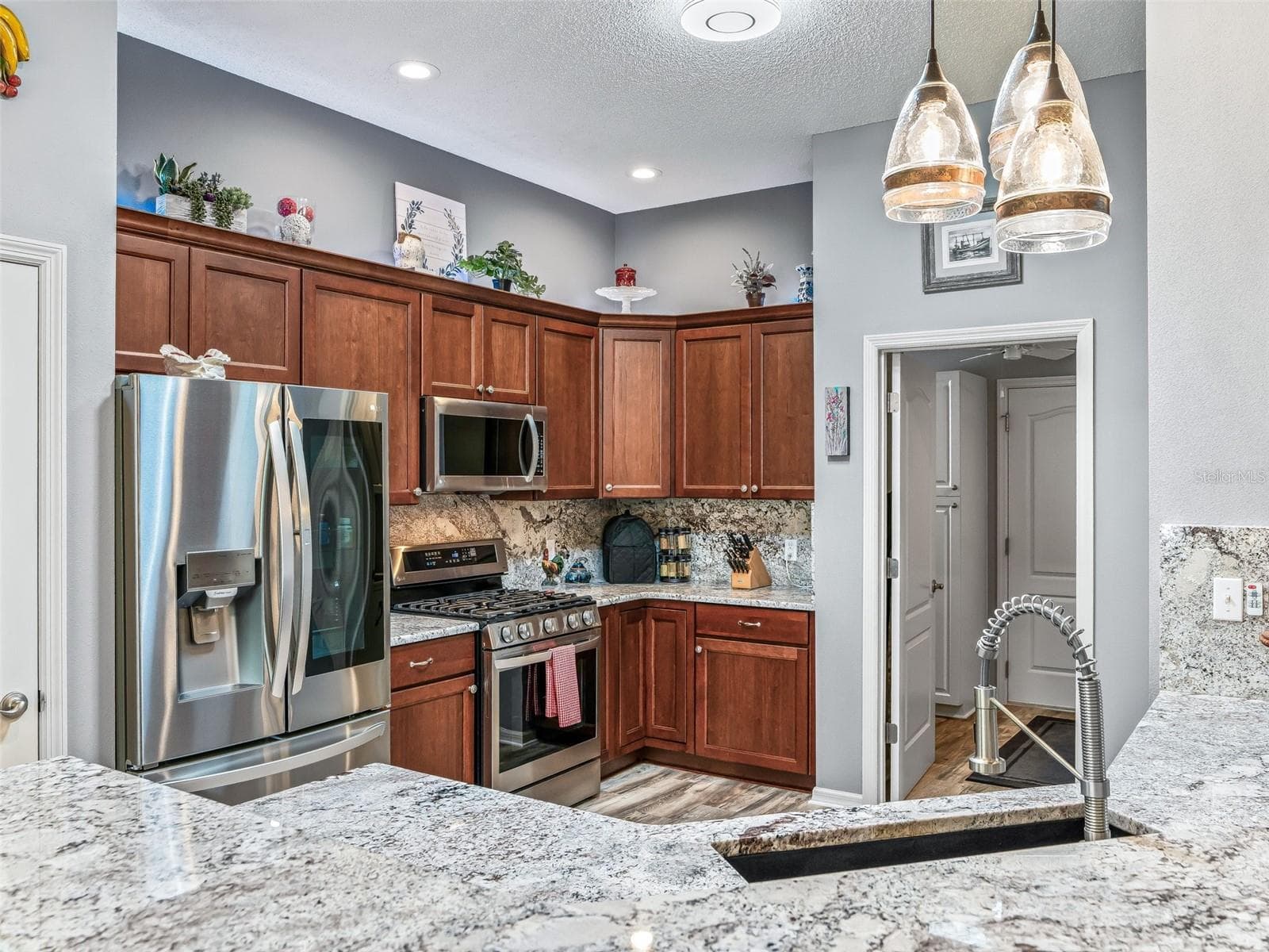 Rich wood cabinetry, granite countertops, stainless steel appliances, decorative backsplash, and pendant lighting create a polished and functional workspace. - 17946 SE 87TH MELROSE CT, THE VILLAGES