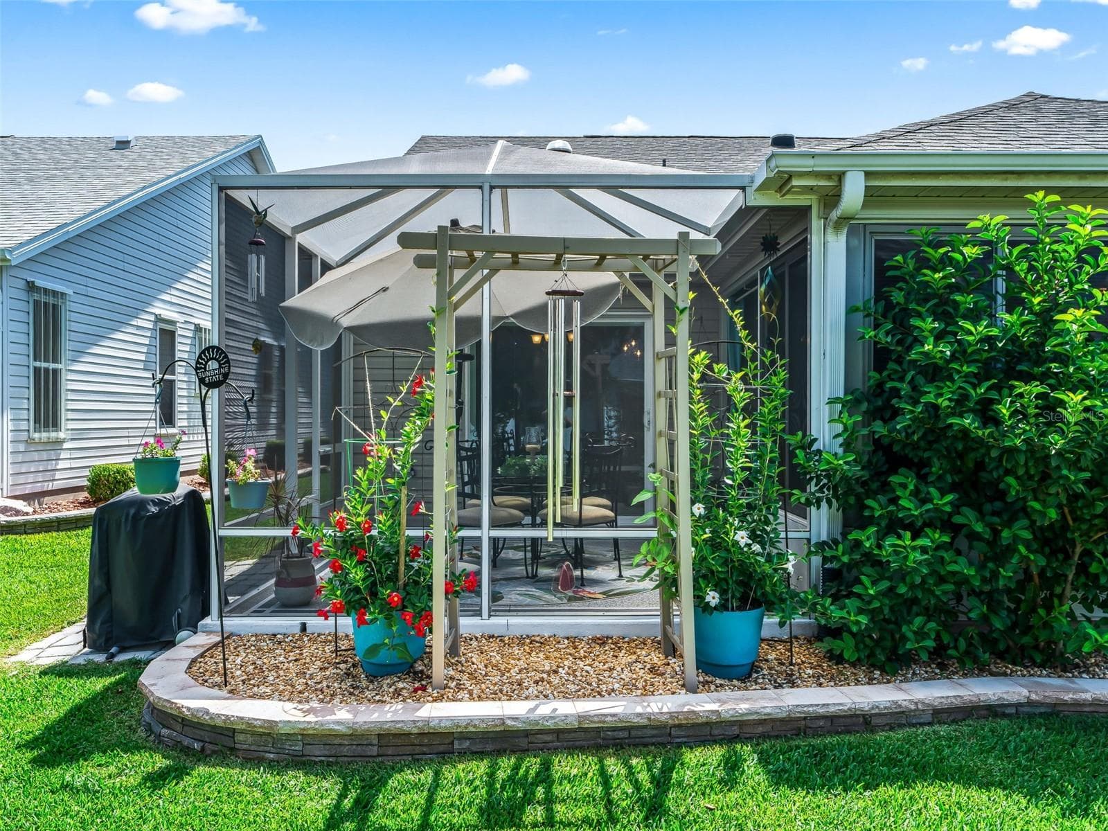 The rear exterior features a partially enclosed lanai with two adjoining covered birdcages- both patios are surrounded by mature landscaping and colorful plantings. - 17946 SE 87TH MELROSE CT, THE VILLAGES
