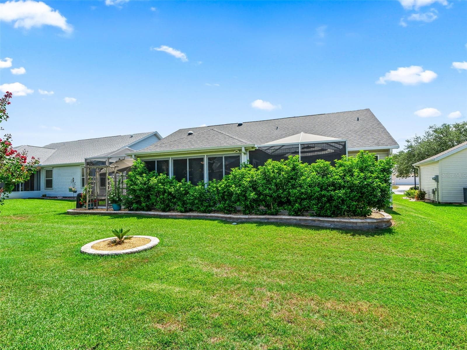 The home’s rear elevation showcases a large screened living area bordered by lush hedges and a beautifully maintained lawn. - 17946 SE 87TH MELROSE CT, THE VILLAGES