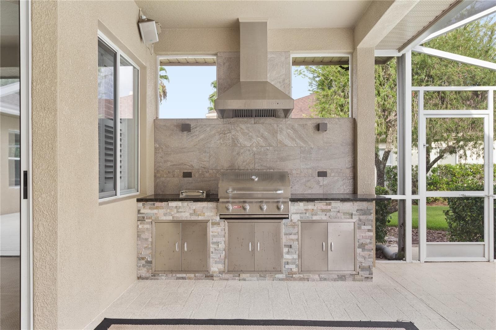 The custom outdoor kitchen features a built-in gas grill, vent hood, and thoughtfully placed lighting that beautifully illuminates the cooking area for effortless day or evening entertaining. - 26920 WINGED ELM DR, WESLEY CHAPEL