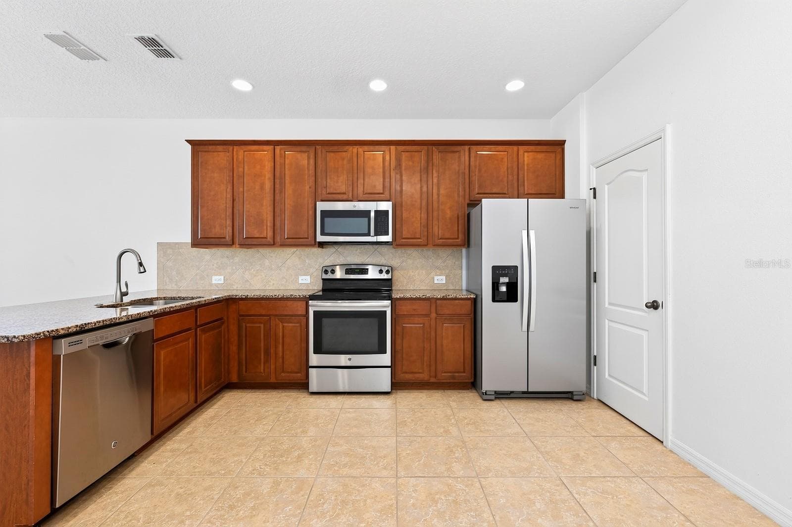 The kitchen is designed to be both functional and inviting, featuring rich cabinetry, granite countertops, a tiled backsplash, STAINLESS STEEL APPLIANCES, pantry storage, and a breakfast bar that overlooks the living and dining areas. - 11429 BROWNSTONE ST, WINDERMERE