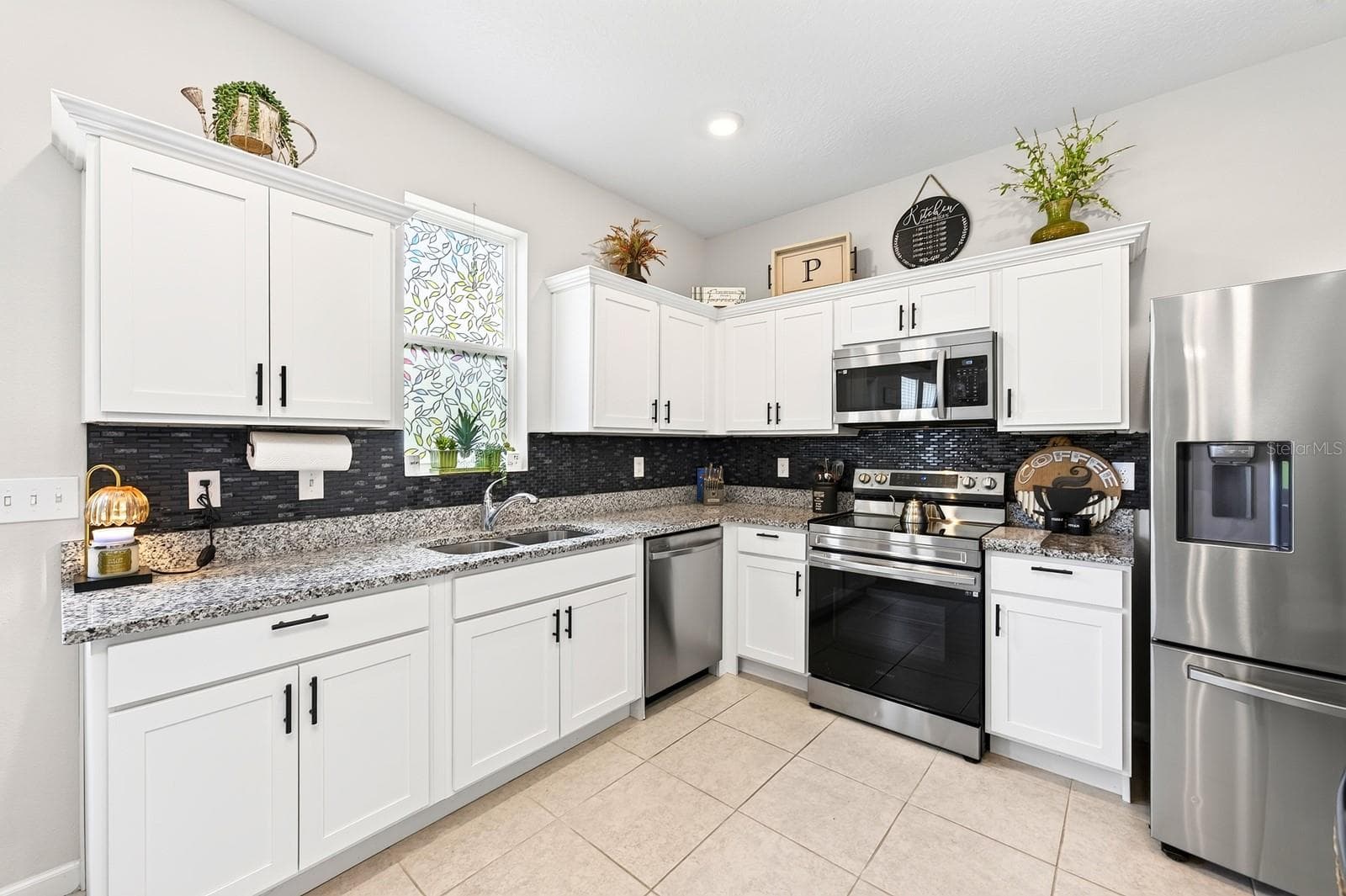 The bright, modern Kitchen is the heart of the home, featuring crisp white cabinetry, GRANITE COUNTERTOPS, stainless steel appliances, a stylish tile backsplash, recessed lighting, and a convenient closet pantry. - 1961 HEMINGWAY CIR, GROVELAND