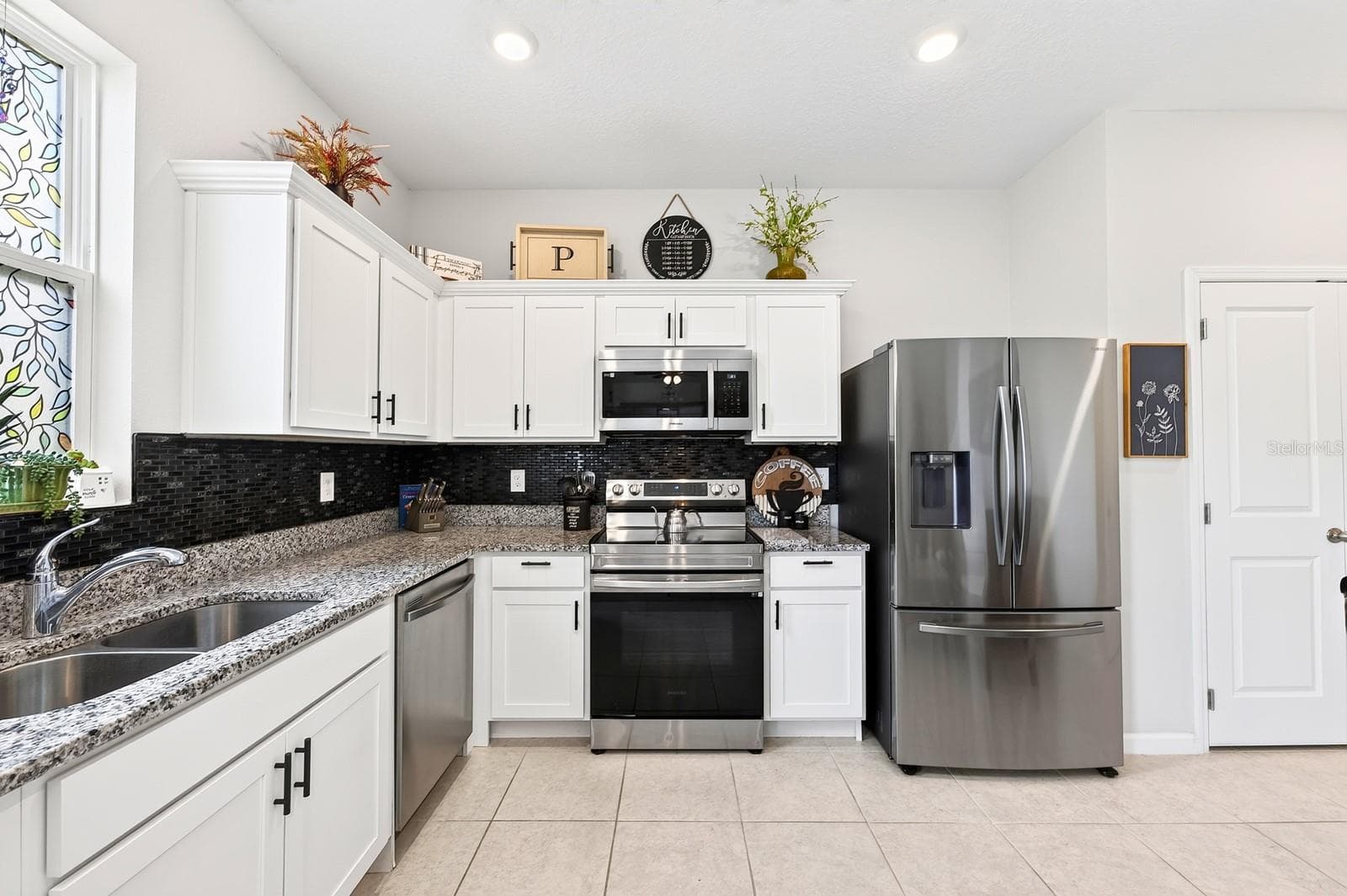 The bright, modern Kitchen is the heart of the home, featuring crisp white cabinetry, GRANITE COUNTERTOPS, stainless steel appliances, a stylish tile backsplash, recessed lighting, and a convenient closet pantry. - 1961 HEMINGWAY CIR, GROVELAND