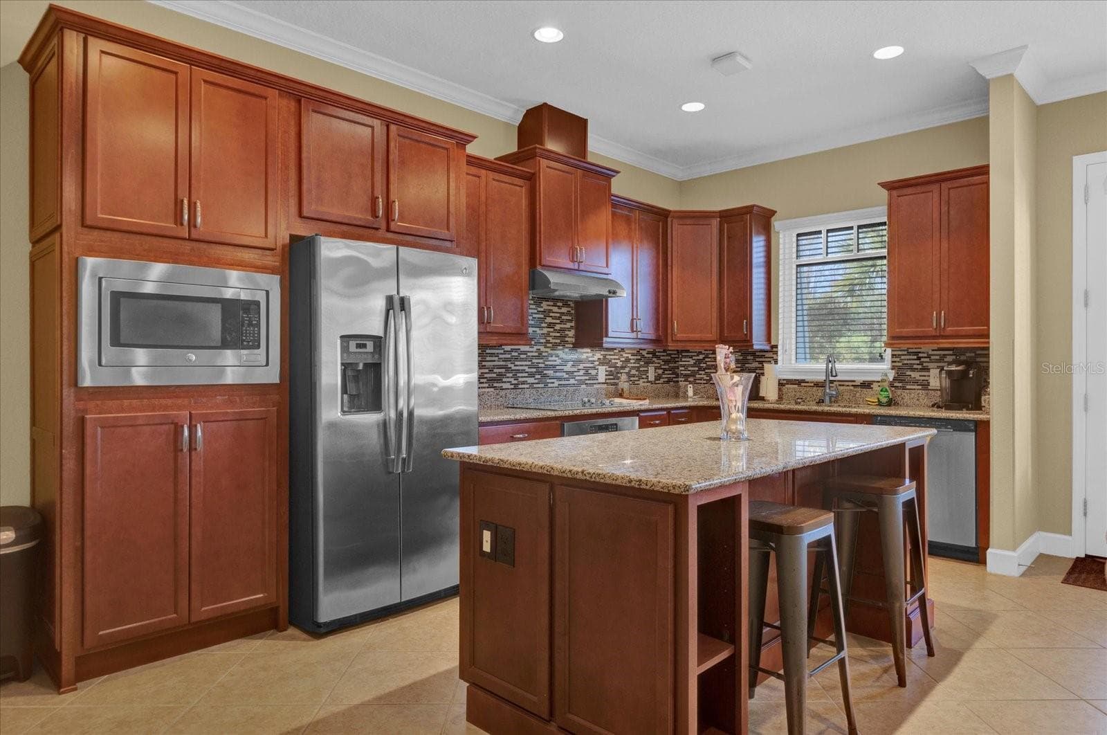 Rich cherry cabinetry paired with stainless steel appliances creates a warm, functional chef's kitchen. - 9219 LAUREATE BLVD, ORLANDO