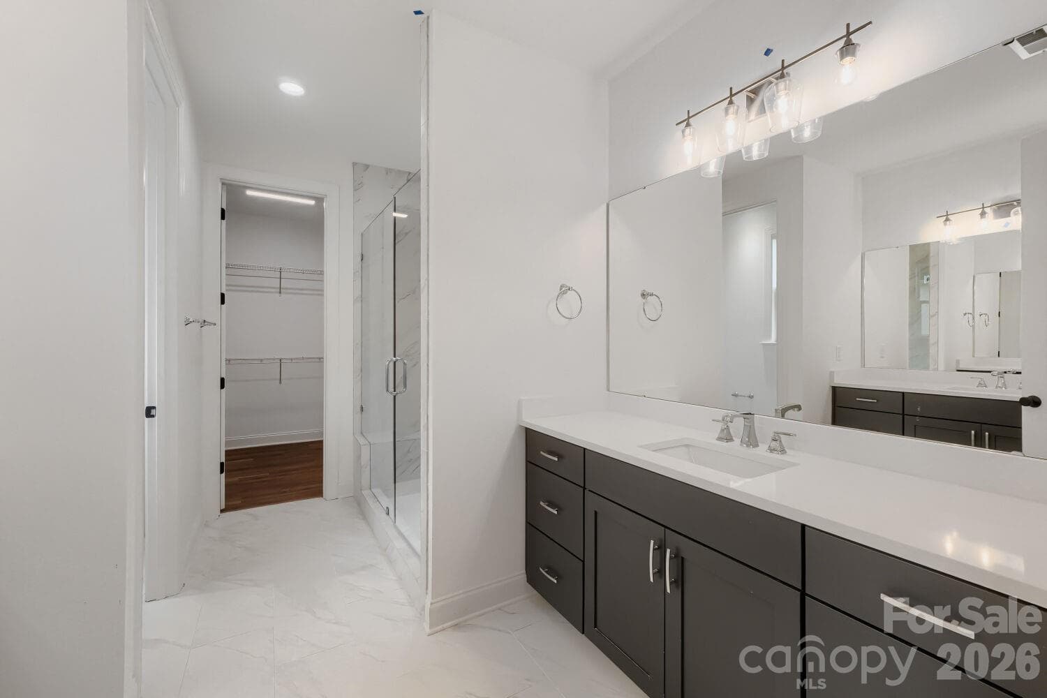 The primary bath offers a dual-vanity setup with contemporary gray cabinetry and a glass-enclosed marble shower. A walk-in closet just off the vanity adds everyday convenience. - 2358 Fay Jones Road, Denver