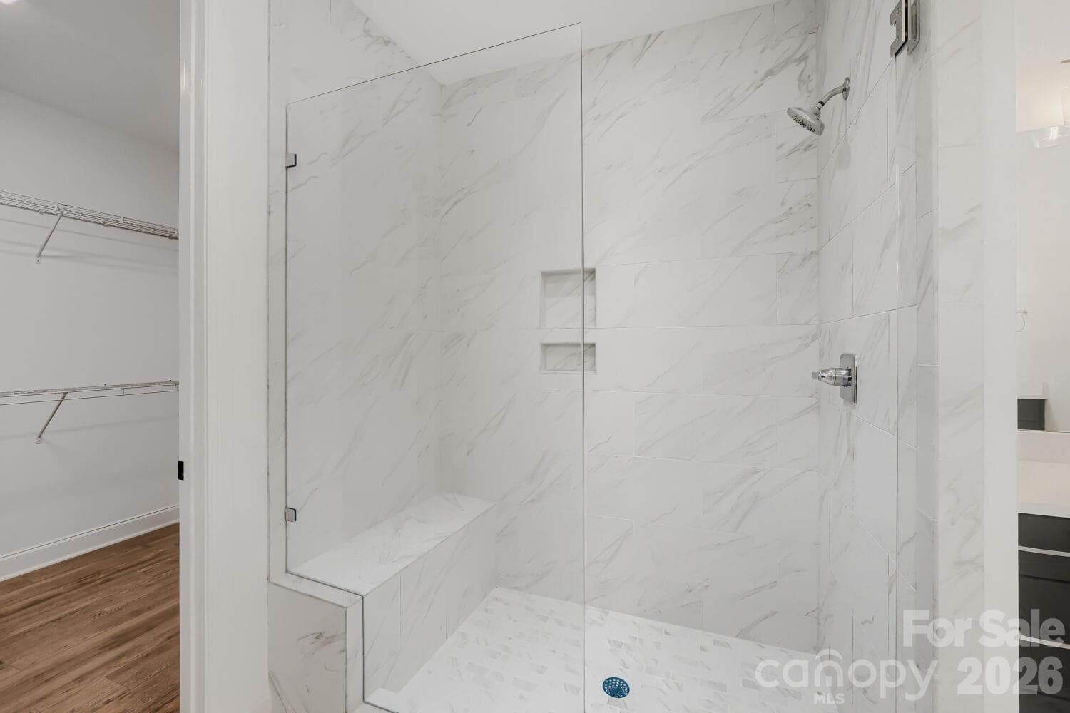 This spa-like walk-in shower is wrapped in marble-look tile with a built-in bench and dual niches. Frameless glass and an adjacent walk-in closet complete the luxurious retreat. - 2358 Fay Jones Road, Denver