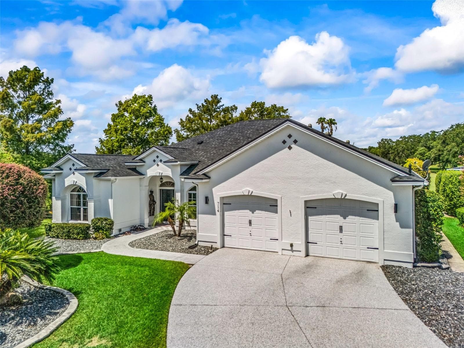 Welcoming front elevation features a wide driveway, three-car garage, manicured lawn, mature landscaping, and classic Premier-home architecture. - 714 CIMARRON AVE, THE VILLAGES