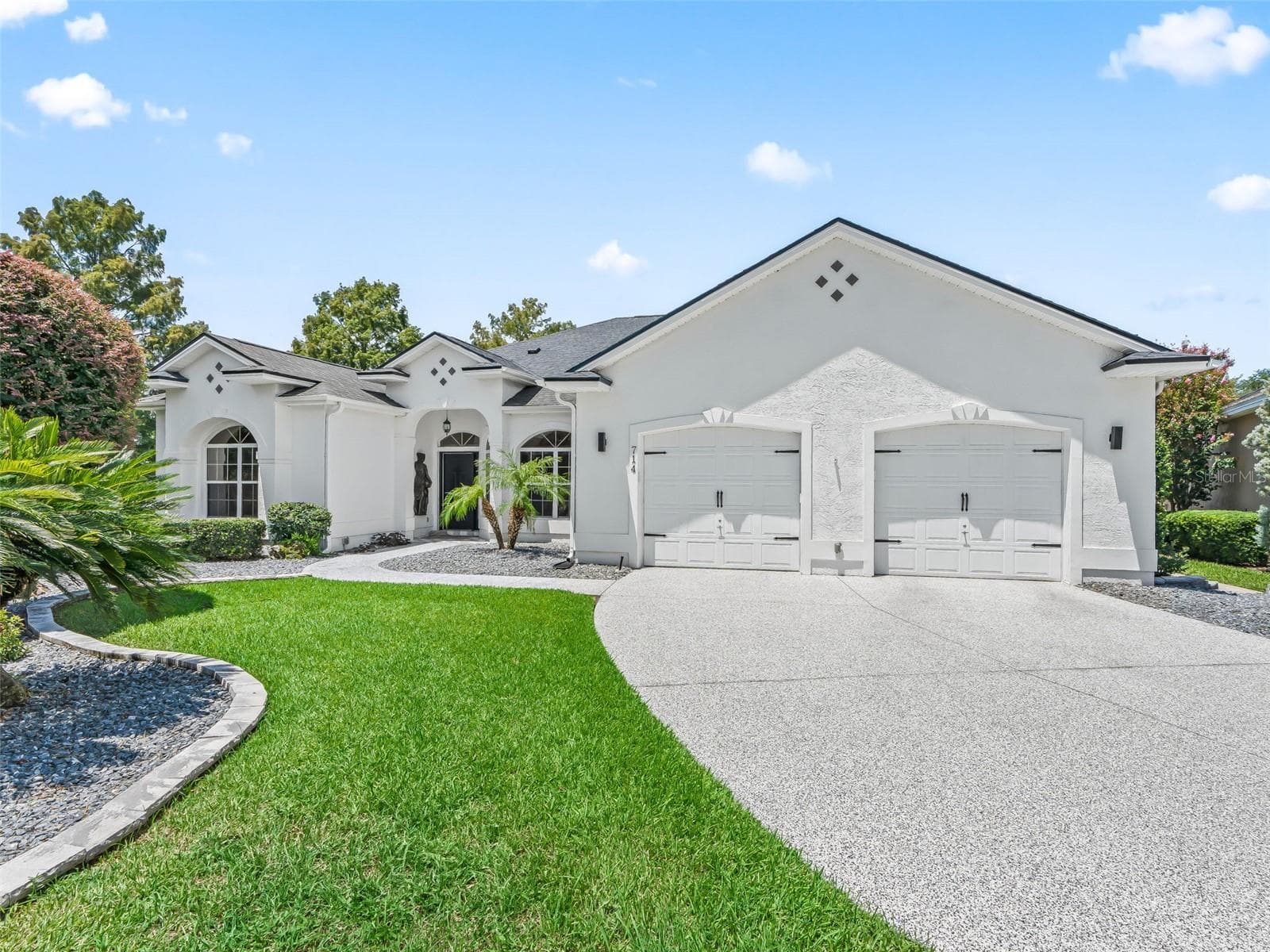 Another attractive exterior perspective showcasing the home's substantial driveway, multiple garage bays, tile-style roofline, and beautifully maintained grounds. - 714 CIMARRON AVE, THE VILLAGES