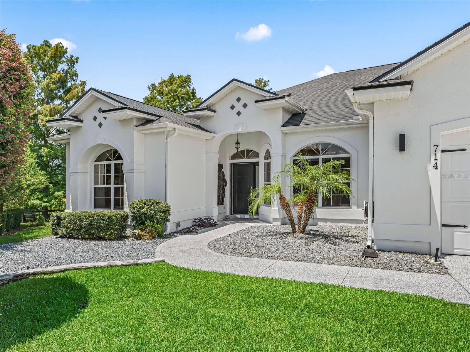 The home's distinctive front entry is framed by graceful architectural details, mature landscaping, and a charming courtyard-style approach that creates an inviting first impression. - 714 CIMARRON AVE, THE VILLAGES