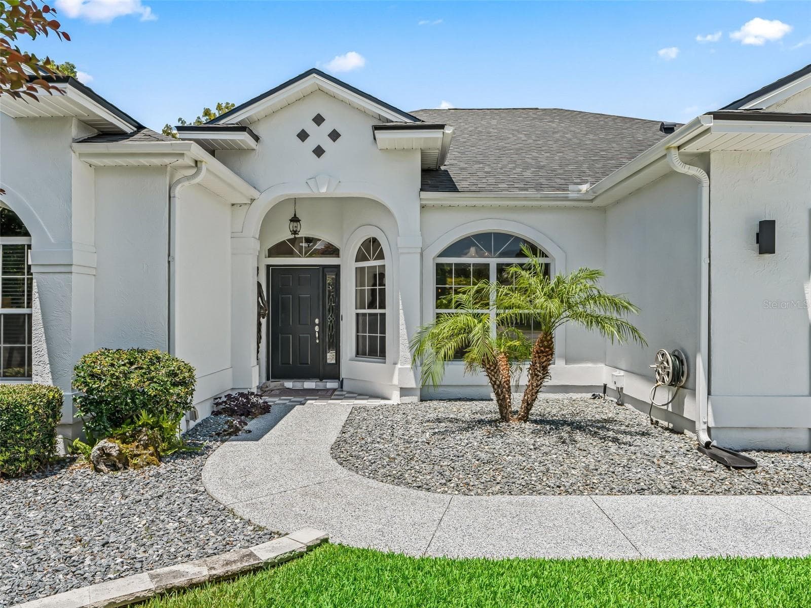Beautifully landscaped entry features a decorative front door, arched architectural accents, and low-maintenance rock landscaping accented by tropical greenery - 714 CIMARRON AVE, THE VILLAGES