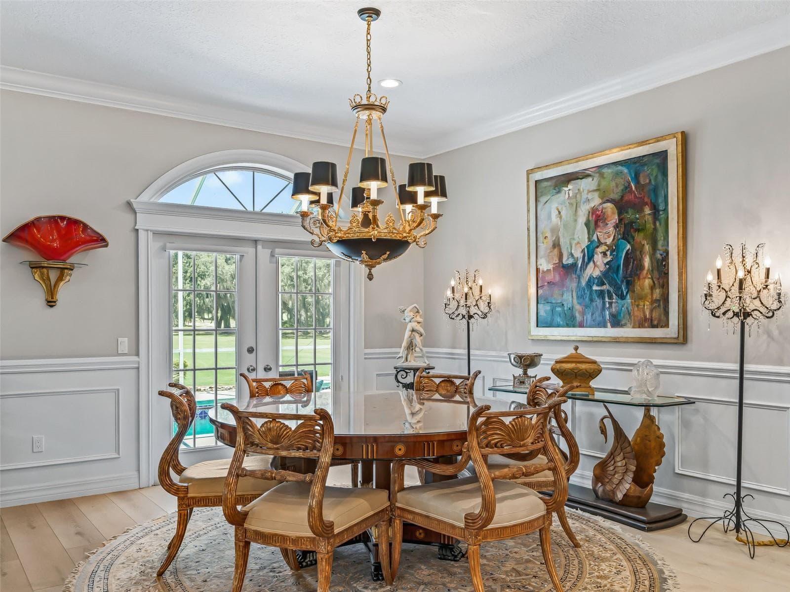 Beautiful dining area features an elegant chandelier, arched window, crown molding, wainscoting, and framed trim details that add to the home's custom Premier character. - 714 CIMARRON AVE, THE VILLAGES