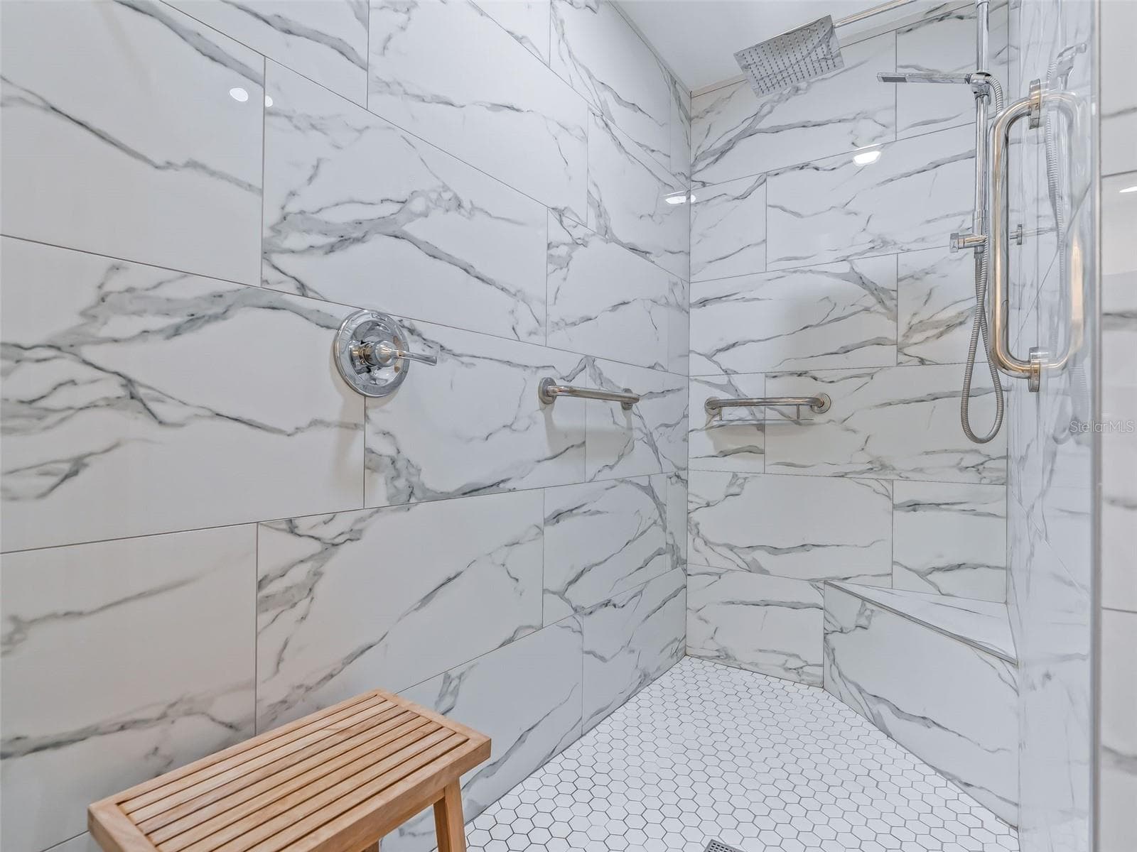 The primary bath features an impressive Roman-style walk-in shower with dramatic marble-look tile, frameless glass, built-in niche, and convenient handheld shower fixture. - 714 CIMARRON AVE, THE VILLAGES
