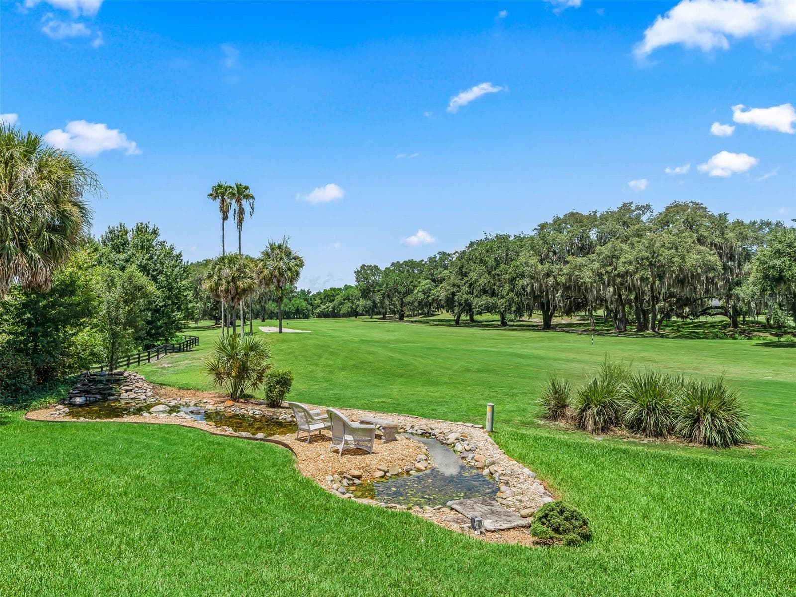 One of the home's standout features is the spectacular long view across the 10th fairway, complemented by a CUSTOM WATERFALL KOI POND, lush landscaping and the peaceful natural backdrop of the Hudson Morse Parr Wildlife Preserve to the left. - 714 CIMARRON AVE, THE VILLAGES