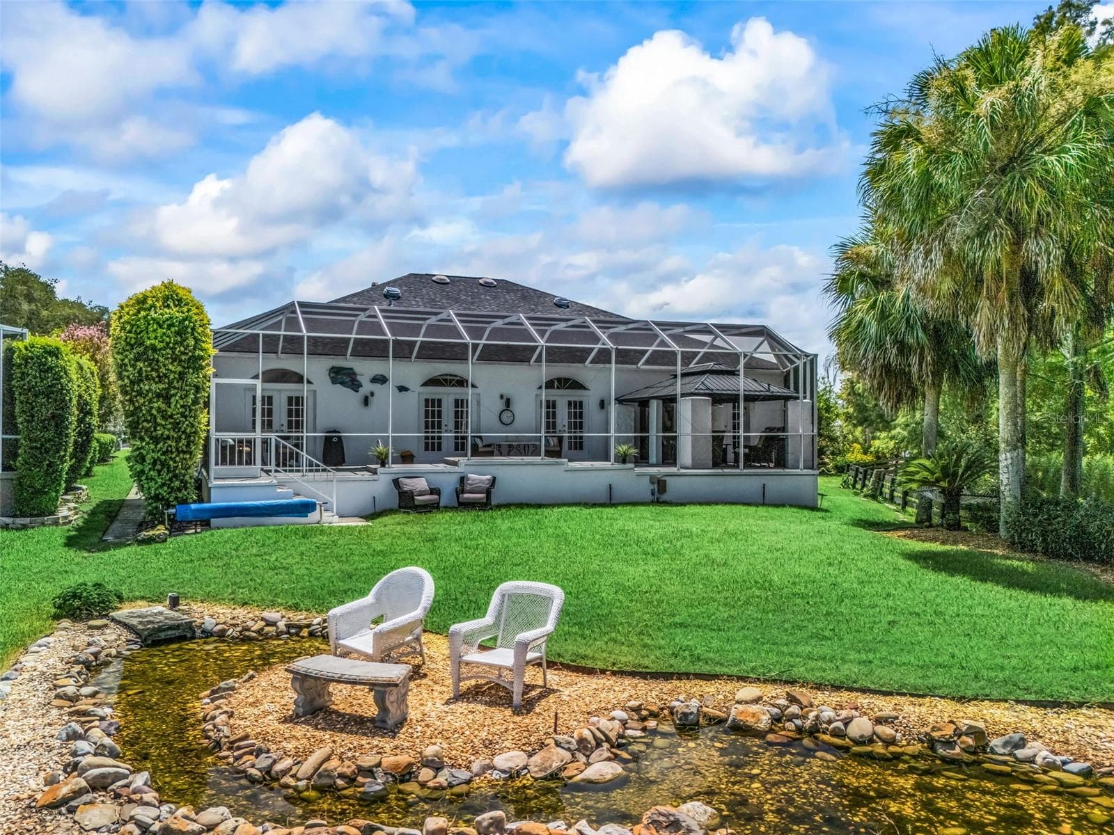 The rear of the home is framed by mature tropical landscaping, open lawn, and peaceful golf course surroundings, highlighting the property's extraordinary privacy. - 714 CIMARRON AVE, THE VILLAGES