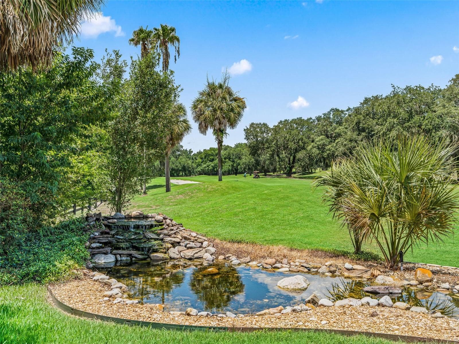 The backyard blends beautifully with the surrounding fairway, featuring mature palms, lush landscaping, and a decorative pond with cascading waterfall. - 714 CIMARRON AVE, THE VILLAGES