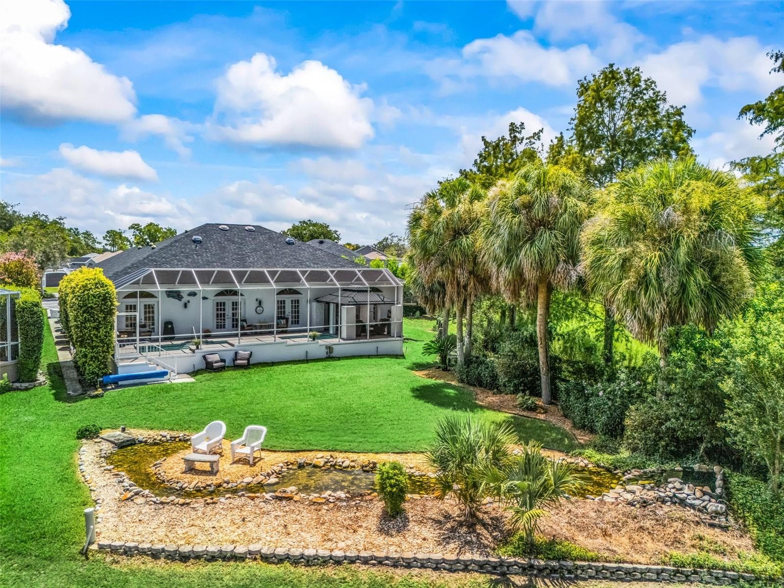 Wide view captures the screened pool area, lush tropical landscaping, backyard seating area, water feature, and lush preserve to the right. - 714 CIMARRON AVE, THE VILLAGES