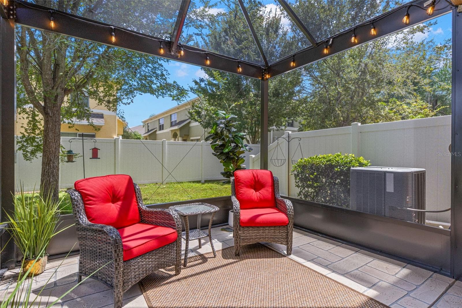 The screened lanai overlooks a small grassy area framed by a vinyl privacy fence and mature trees, adding a welcome sense of separation from neighboring homes. - 9524 TRUMPET VINE LOOP, NEW PORT RICHEY