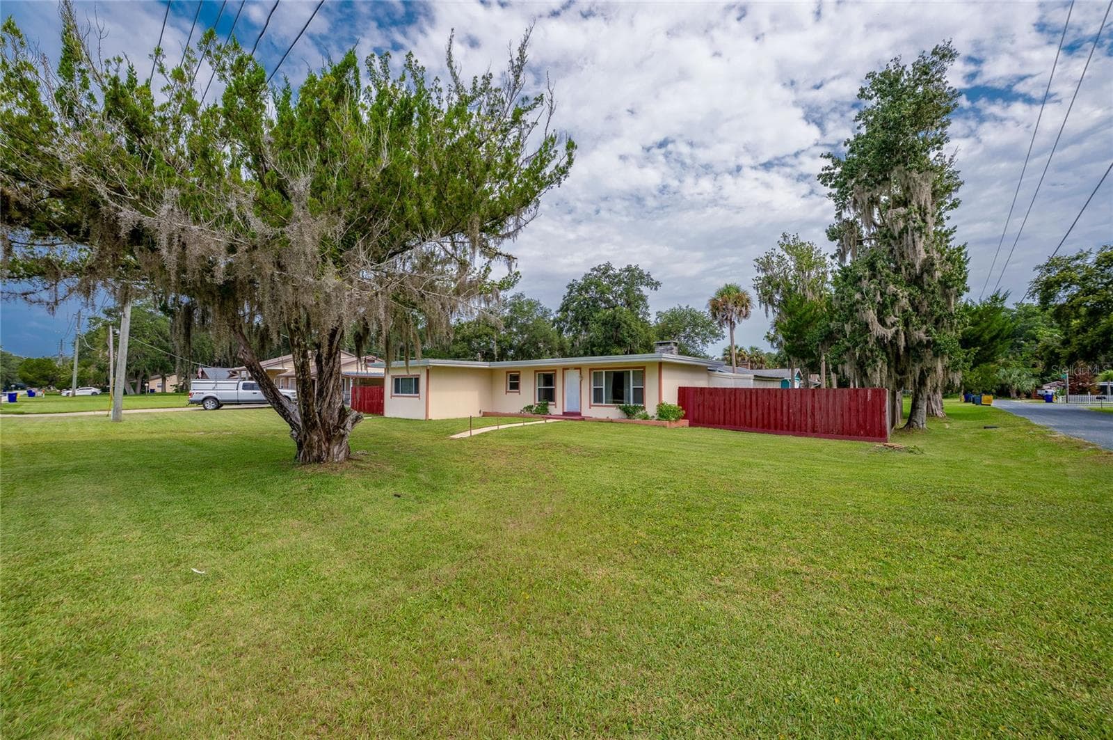 Single-story home framed by expansive green lawns, mature shade trees draped in Spanish moss, and a crimson perimeter fence. - 1101 16TH ST, EDGEWATER