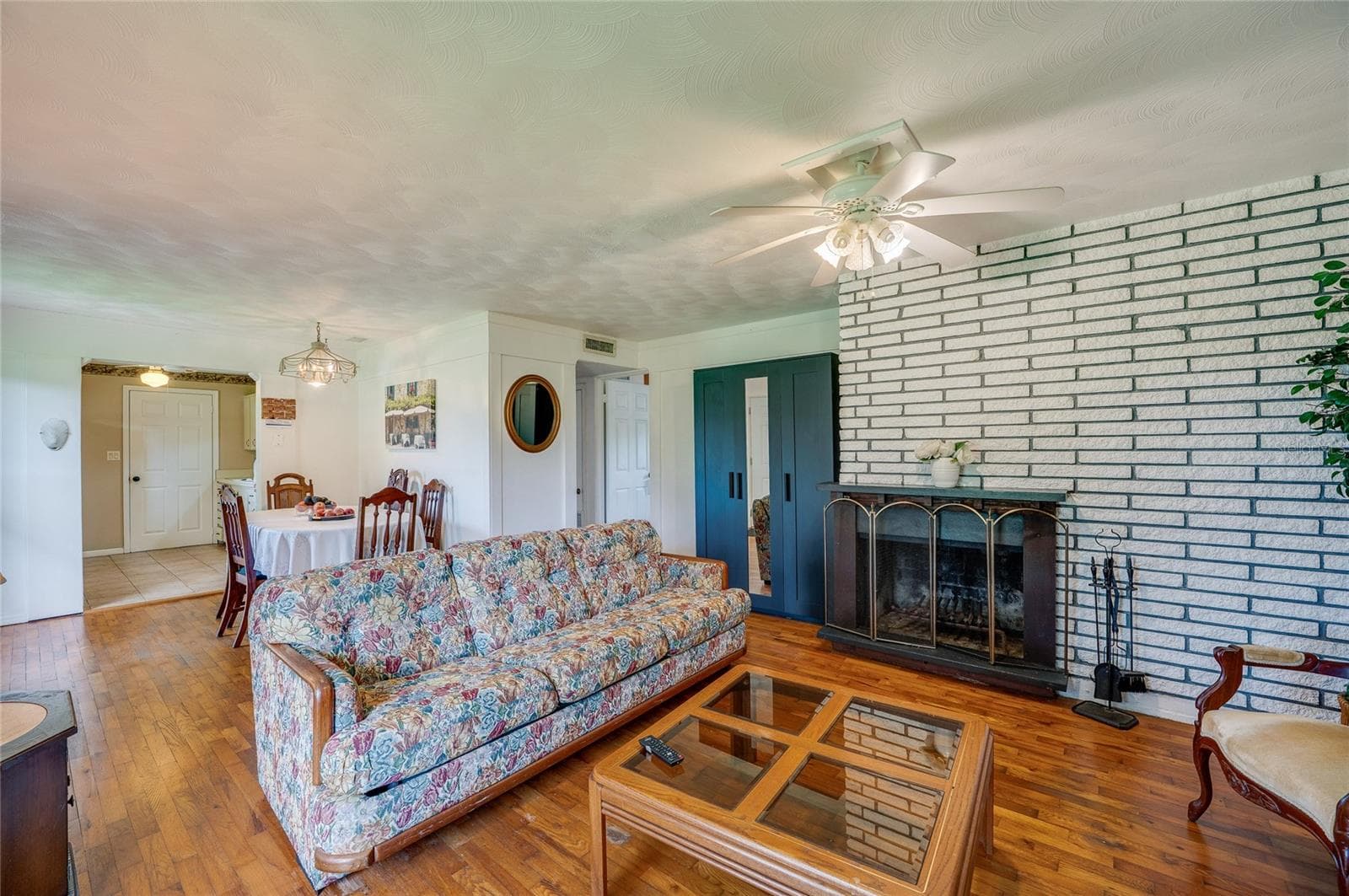 Open-concept main living space featuring rich wood flooring, a central ceiling fan, and a painted brick fireplace. The seamless floor plan connects adjacent living zones. - 1101 16TH ST, EDGEWATER